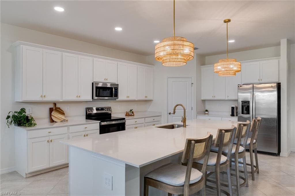 Spacious kitchen featuring an expansive island with seating, white shaker-style cabinetry, stainless steel appliances, and two decorative pendant lights