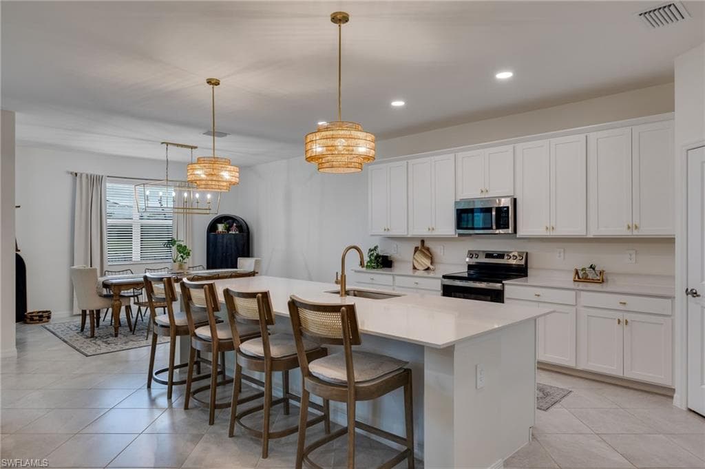 Spacious kitchen featuring an expansive island with seating, white shaker cabinetry, stainless steel appliances, and light-toned tile flooring