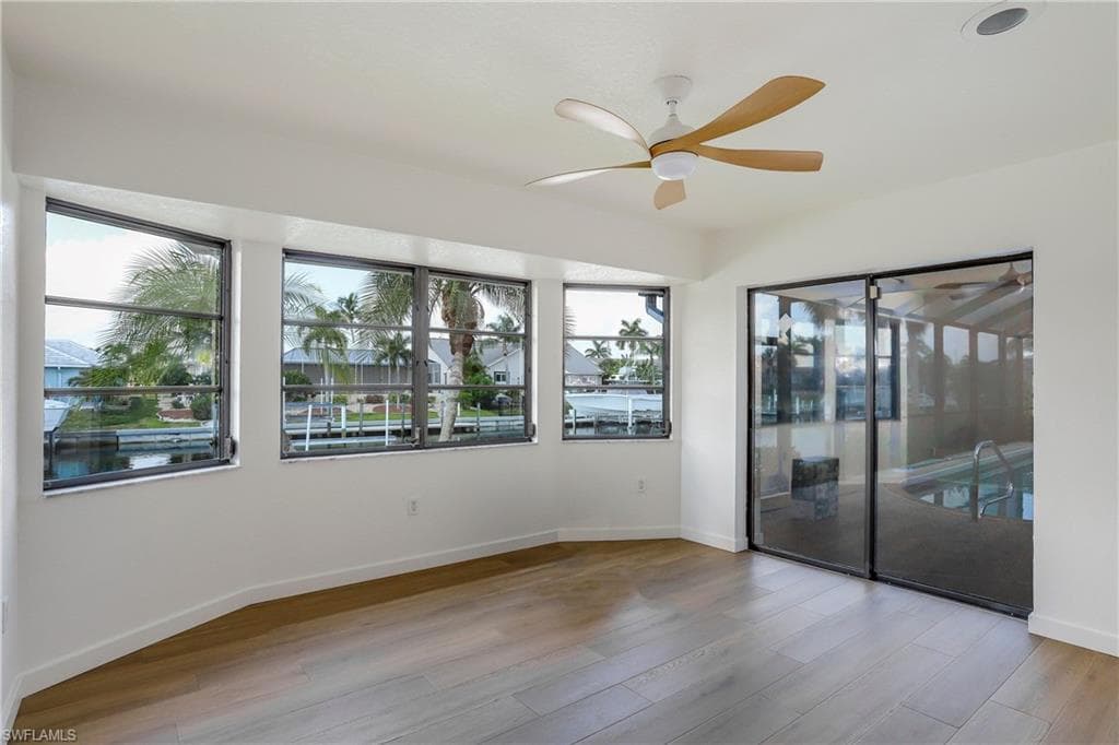 Waterfront room featuring multiple windows with canal views, wood-finish flooring, a ceiling fan, and sliding glass doors opening to a screened pool enclosure