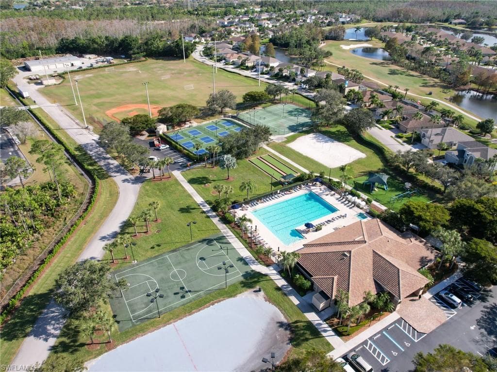 Aerial perspective showcasing community amenities including a large swimming pool, multi-court sports complex, multiple tennis courts, and a sand volleyball court