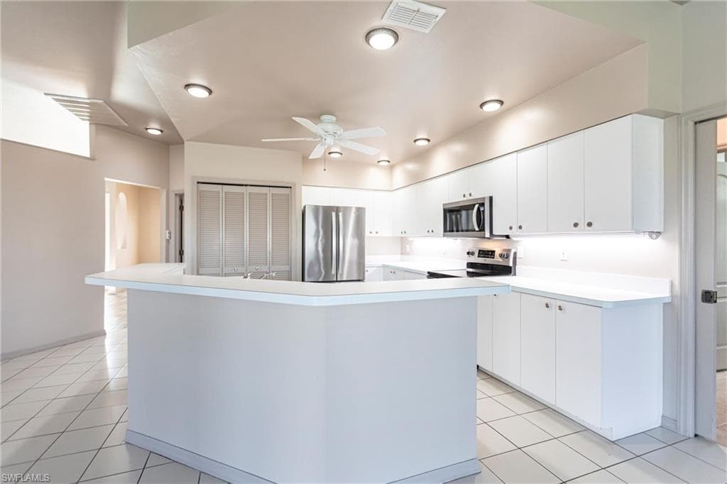 Kitchen with stainless steel appliances, light tile patterned flooring, a kitchen island with sink, and white cabinets.