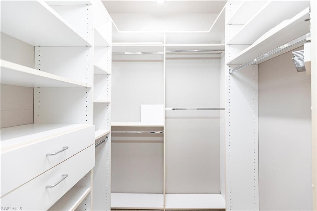View of spacious custom (Closets-by-Design) neutral carpeted closet with two drawers and adjustable shelving and racks.