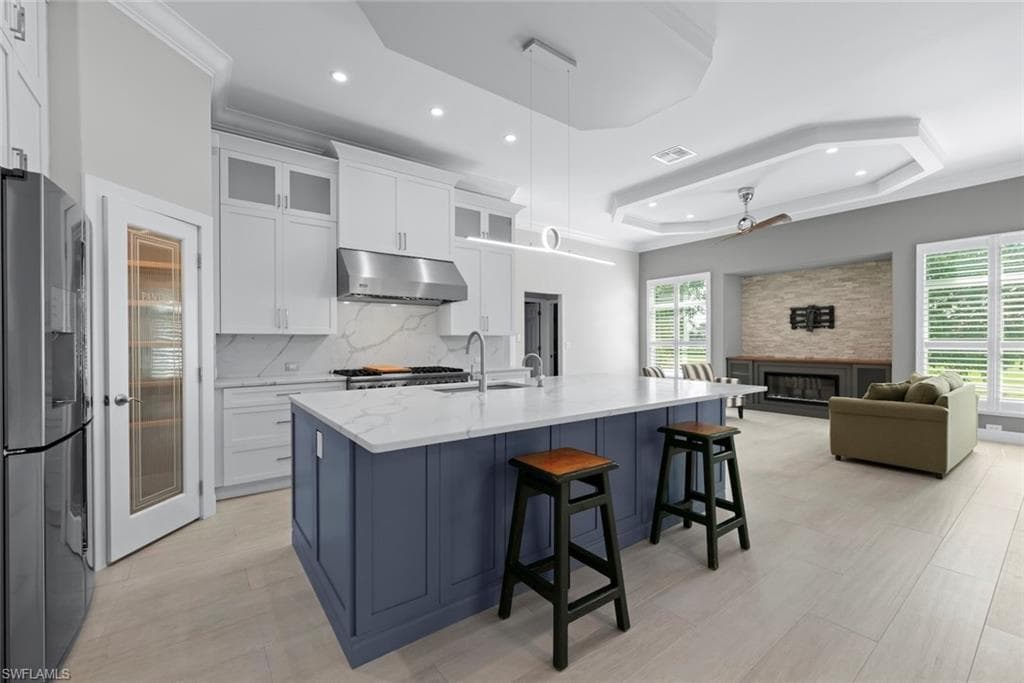 Modern kitchen featuring a large island with white countertops and a blue base, stainless steel appliances, and white cabinetry