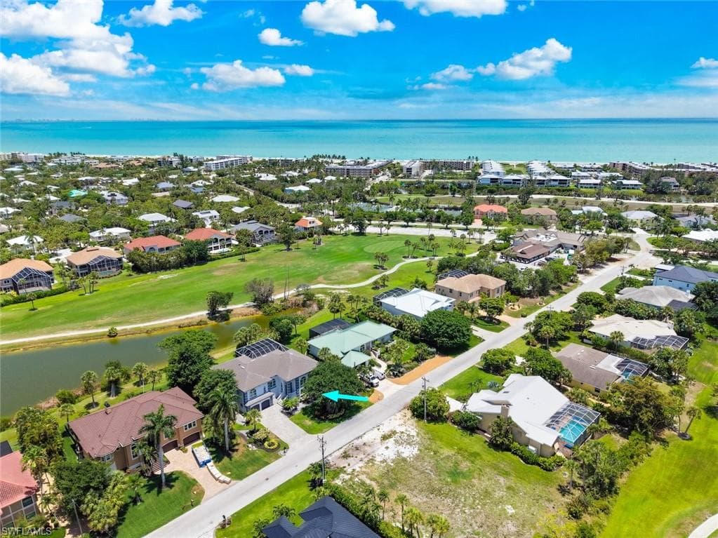 Aerial perspective showcasing a residential neighborhood with verdant landscaping, offering proximity to a golf course, a body of water, and the distant ocean