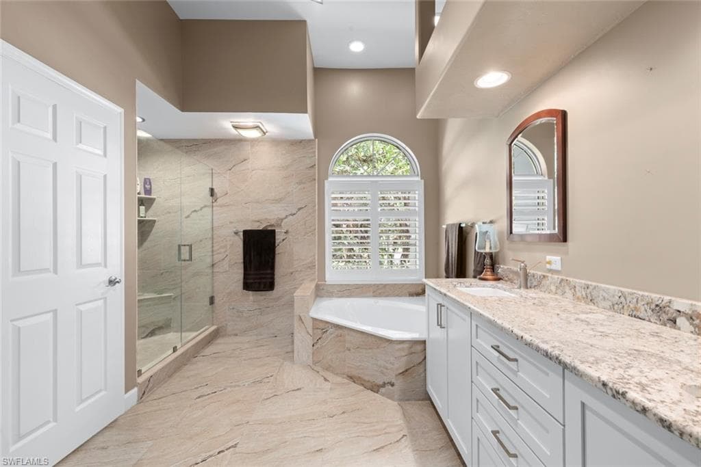 Spacious bathroom featuring a glass-enclosed shower, a corner built-in soaking tub, and an arched window with plantation shutters