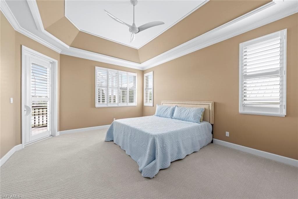 Spacious room featuring a tray ceiling with crown molding, light neutral-toned carpet, and a ceiling fan