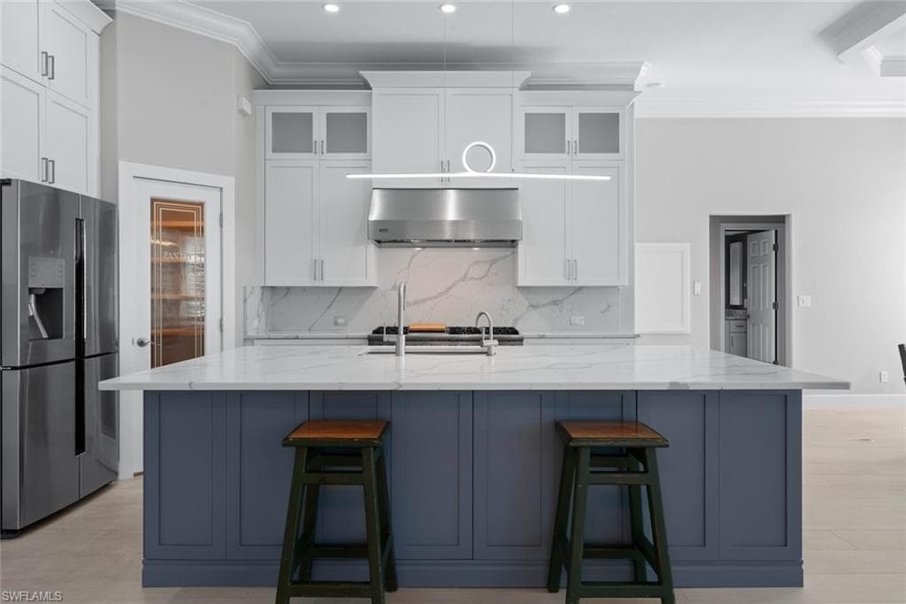 Gourmet kitchen featuring a large central island with a quartz countertop, stainless steel appliances, white cabinetry with glass inserts, and a decorative pendant light fixture