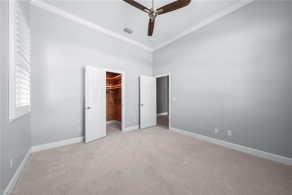 Carpeted interior room featuring a ceiling fan, crown molding, plantation shutters, and a walk-in closet with built-in shelving