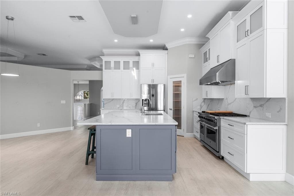 Modern kitchen featuring a large central island with a contrasting base, white shaker-style cabinetry, stainless steel appliances, marble-look countertops and backsplash, and recessed lighting
