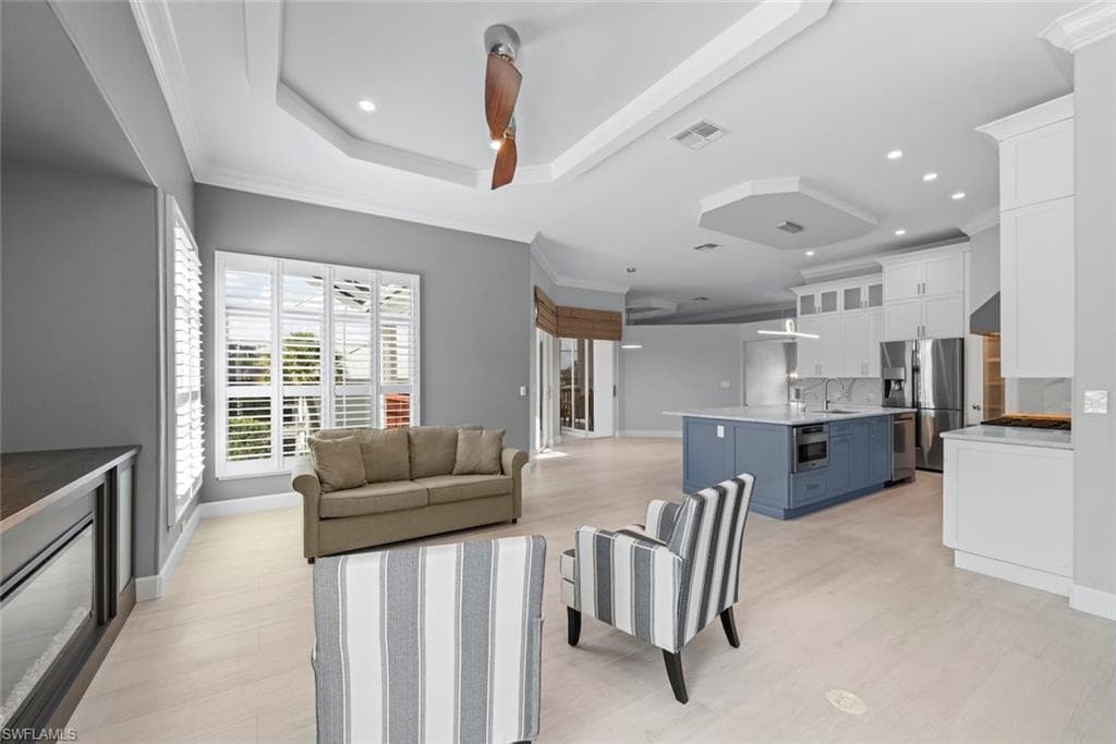 Open-concept living space featuring light wood-finish flooring, recessed lighting, and tray ceilings
