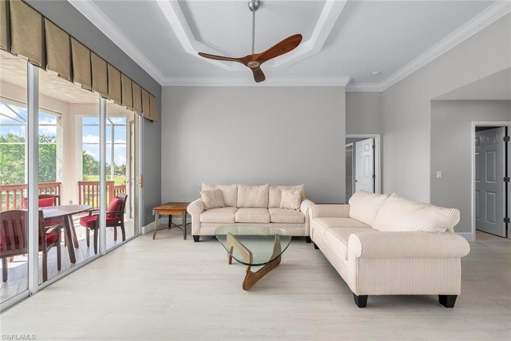 Spacious interior featuring light wood-finish flooring, a tray ceiling with a ceiling fan, and crown molding
