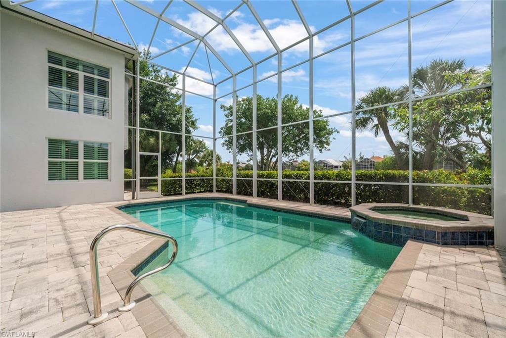 Screened pool area featuring a rectangular swimming pool, integrated spa with waterfall, and paver decking