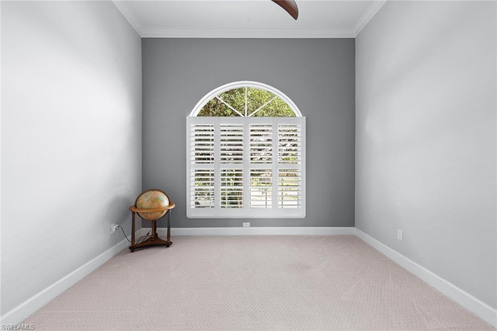 Room featuring an arched window with plantation shutters, light-colored carpeting, a ceiling fan, and crown molding