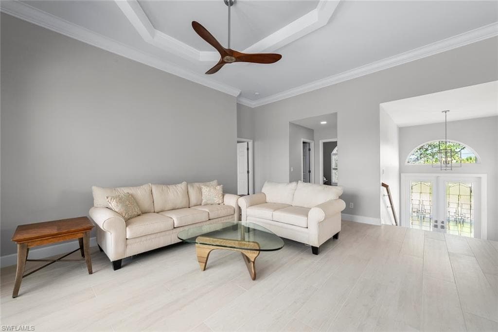 Spacious living area featuring light-toned wood-finish flooring and a tray ceiling with a ceiling fan