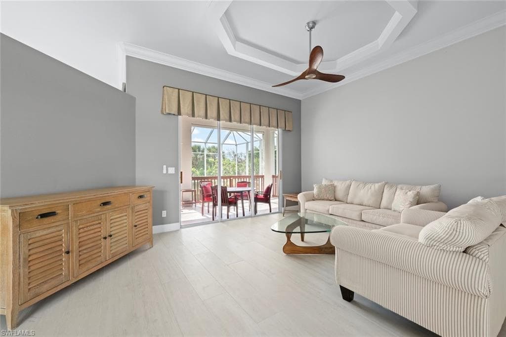 Spacious living area featuring light wood-finish flooring, a contemporary ceiling fan, and a tray ceiling