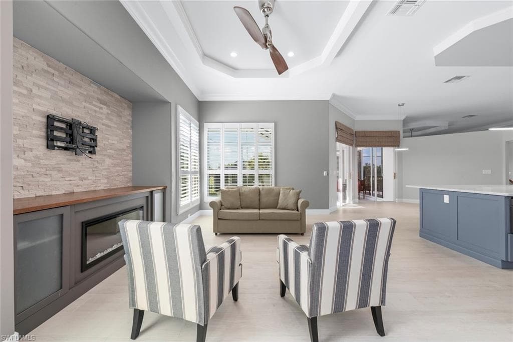 Spacious living area featuring light wood-finish flooring, a tray ceiling with recessed lighting and a ceiling fan, and a built-in media console with an electric fireplace