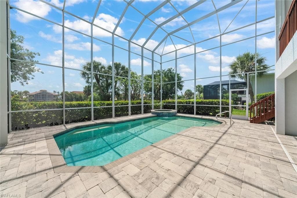Screened outdoor pool area featuring a rectangular pool with an integrated spa, paver decking, and a privacy hedge