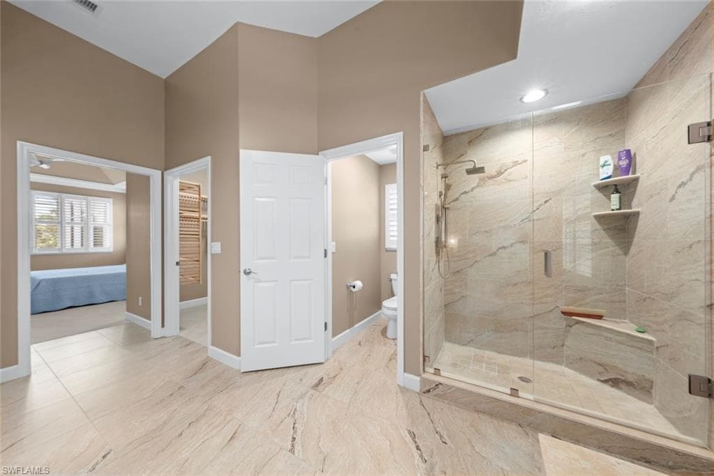 Spacious bathroom featuring large format stone-look tile flooring, a walk-in shower with glass enclosure, built-in shower bench, and recessed lighting