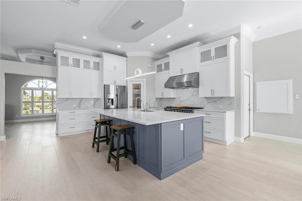 Contemporary kitchen featuring a large central island, light wood-finish flooring, white upper and lower cabinetry, stainless steel appliances, and a tray ceiling