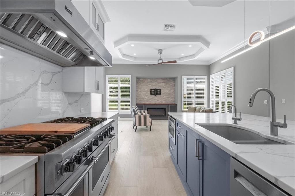 Gourmet kitchen featuring a stainless steel range with a professional-grade hood, white cabinetry, and a large central island with a double sink