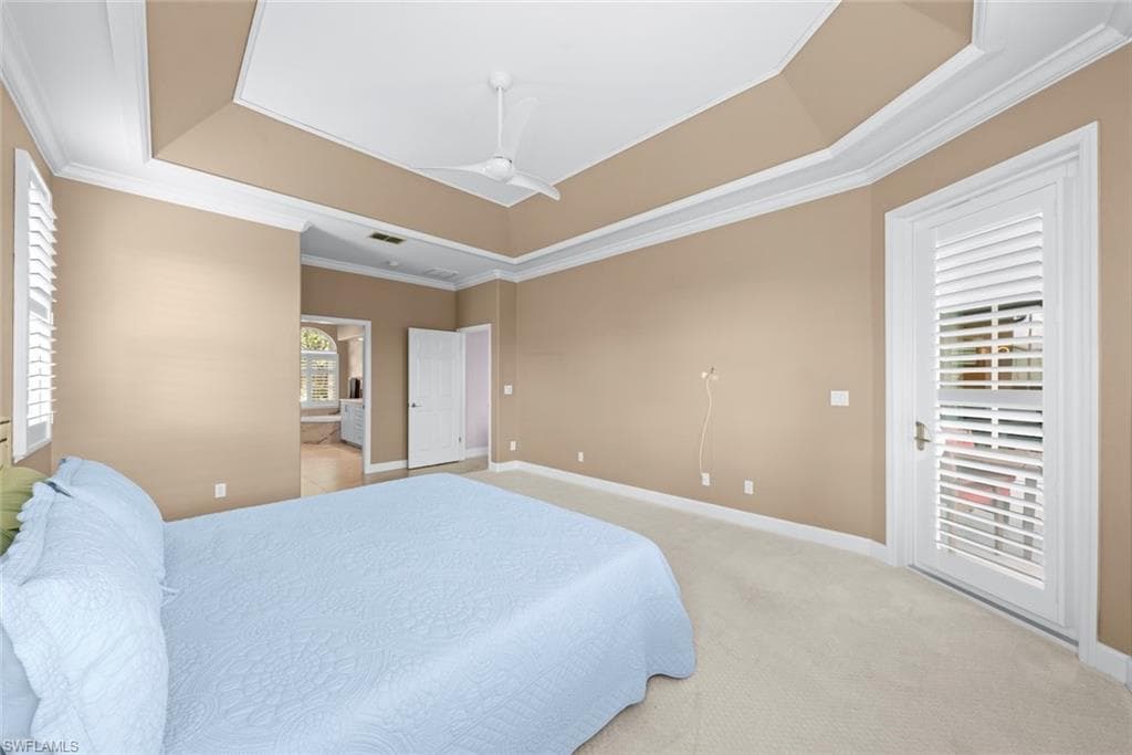 Carpeted interior space featuring a tray ceiling with crown molding, a ceiling fan, and plantation shutters on the window and door
