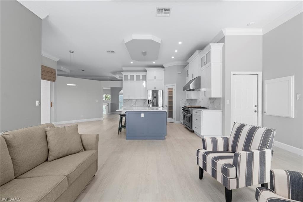Open-concept living area featuring light wood-finish flooring, recessed lighting, and crown molding