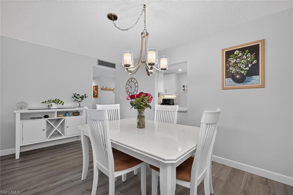 Dining area featuring wood-finish flooring, a contemporary chandelier, a built-in buffet with wine storage, and a pass-through opening