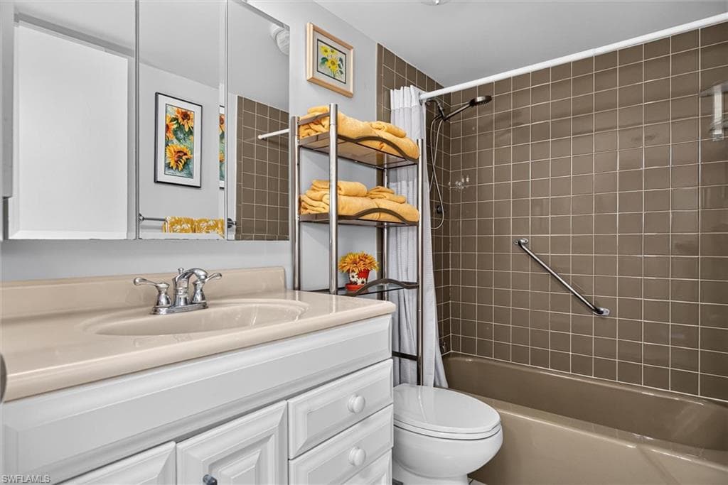 Full Guest Bathroom featuring an integrated sink vanity with white cabinetry, a three-panel mirrored medicine cabinet, a tiled shower surround, and a built-in grab bar