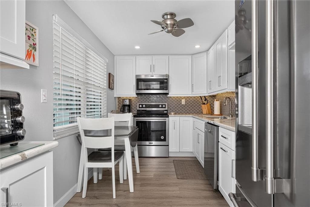 Kitchen featuring white cabinetry, stainless steel appliances, wood-finish flooring, a mosaic tile backsplash, and recessed lighting
