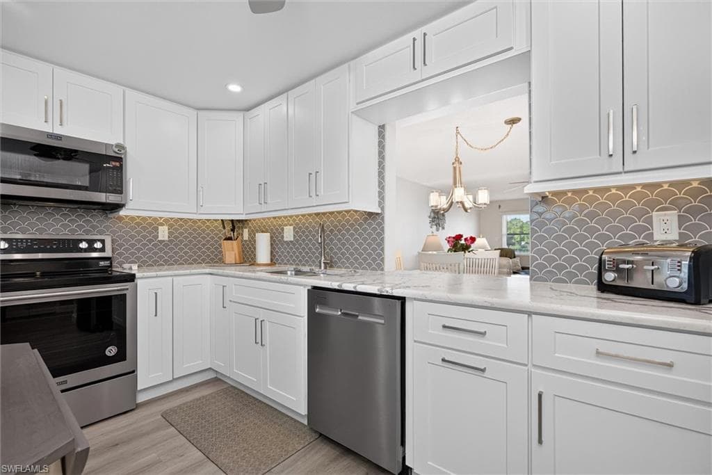 Kitchen featuring white cabinetry, stainless steel appliances, a scalloped tile backsplash, and light-toned countertops