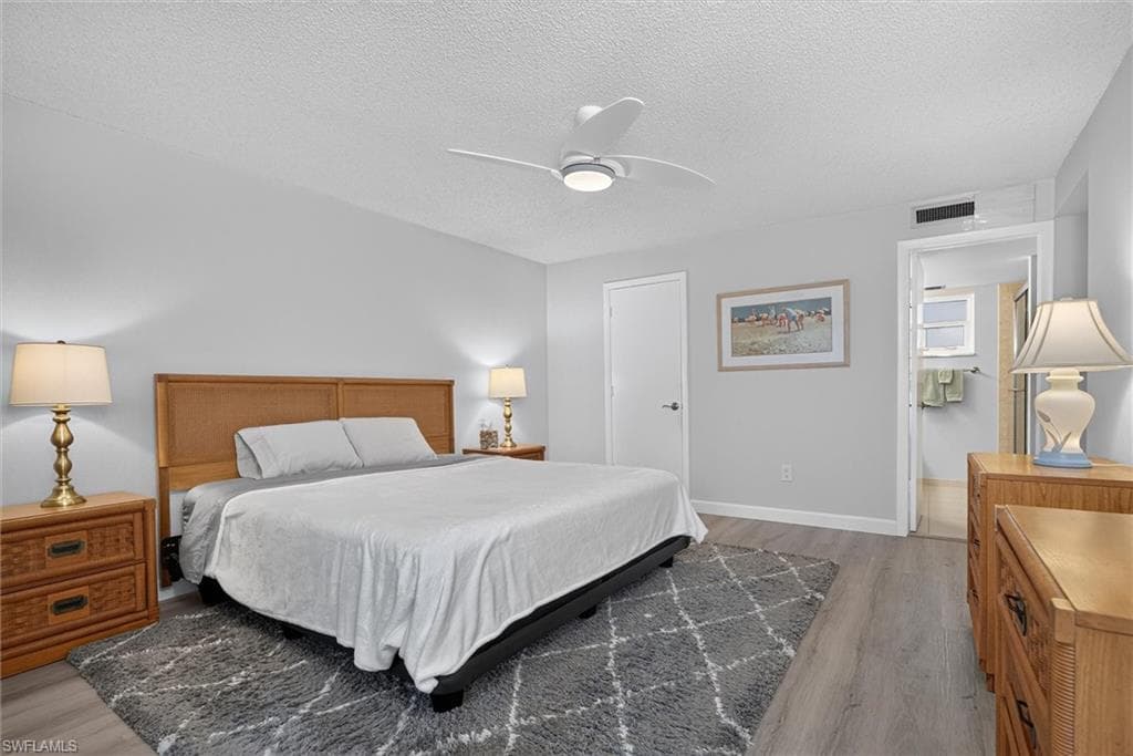 Master Bedroom featuring light-toned walls, wood-finish flooring, a ceiling fan with integrated lighting, and an entryway with a door
