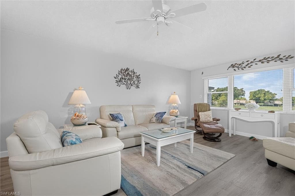 Spacious living area featuring expansive windows, wood-finish flooring, a ceiling fan, and light gray wall tones