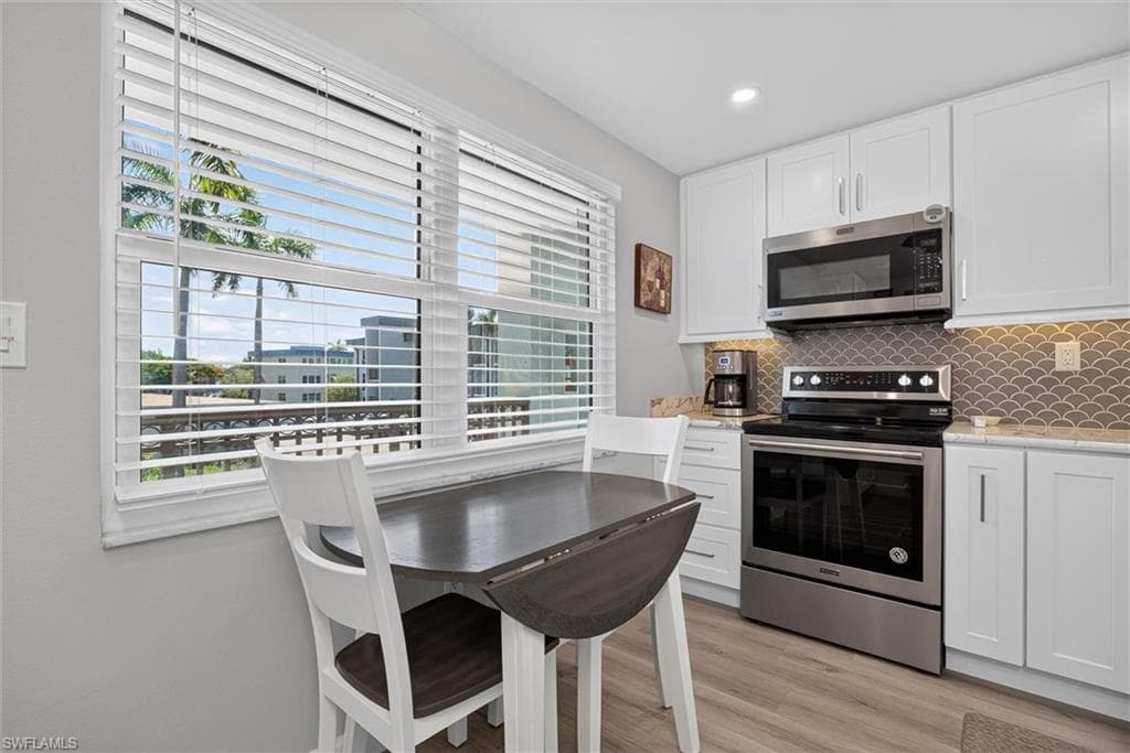 Modern kitchen featuring white cabinetry, stainless steel appliances, a scalloped tile backsplash, and wood-finish flooring