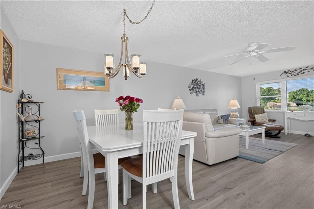 Open-concept living area with wood-finish flooring, a contemporary chandelier, ceiling fan, and large windows