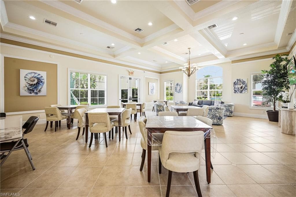Spacious gathering room featuring light-toned tile flooring, tray ceilings with recessed lighting, and expansive windows