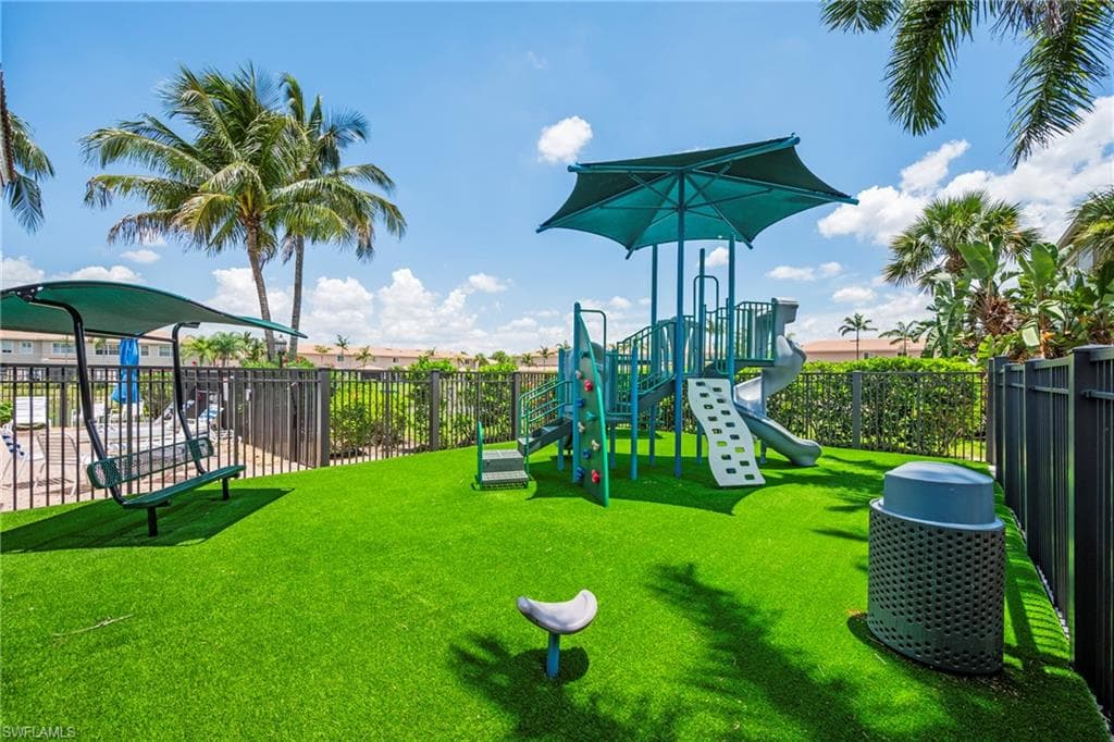 Recreational area featuring a playground structure with slides and climbing elements, a covered swing, and artificial turf surfacing