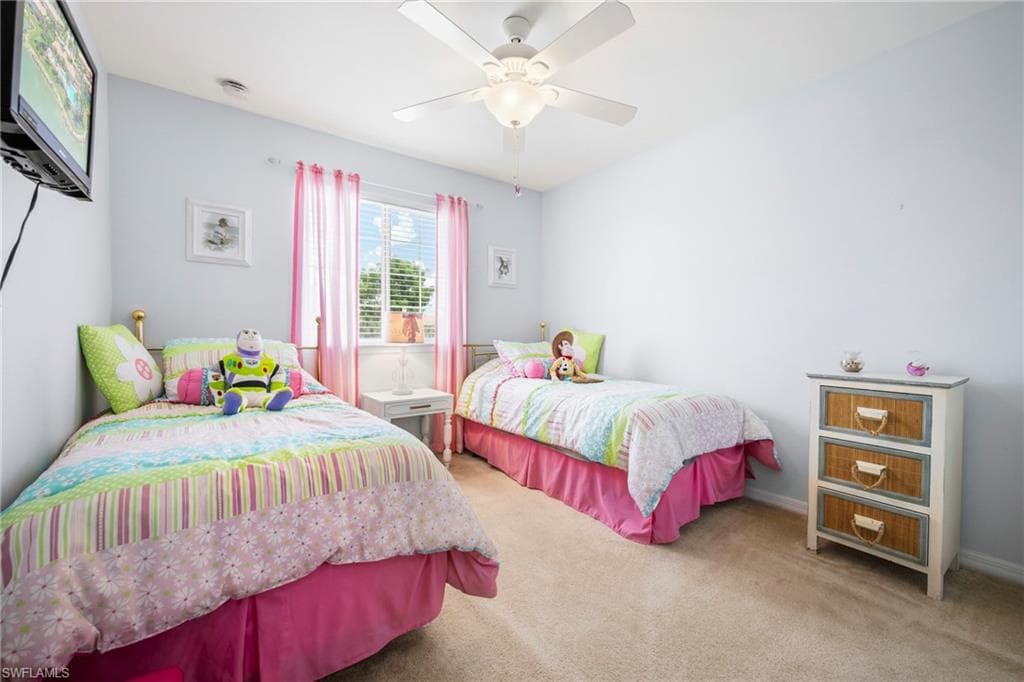 Bedroom featuring light blue walls, window with blinds and pink sheer curtains, beige carpet flooring, and a ceiling fan with integrated lighting