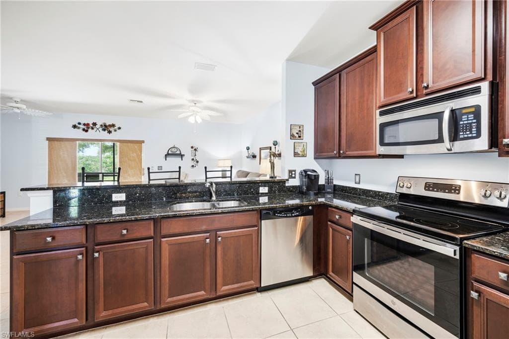 Kitchen featuring dark wood cabinetry, a double basin sink, stainless steel appliances, and dark speckled countertops