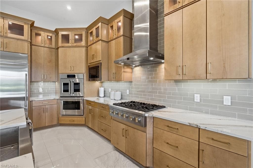 Kitchen featuring stainless steel appliances, stone countertops, light wood-finish cabinetry, a subway tile backsplash, and a gas range