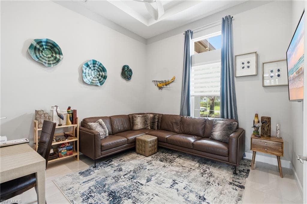 Living area featuring a tray ceiling with a ceiling fan, a large window with blinds and drapes, light-colored walls, and tile flooring
