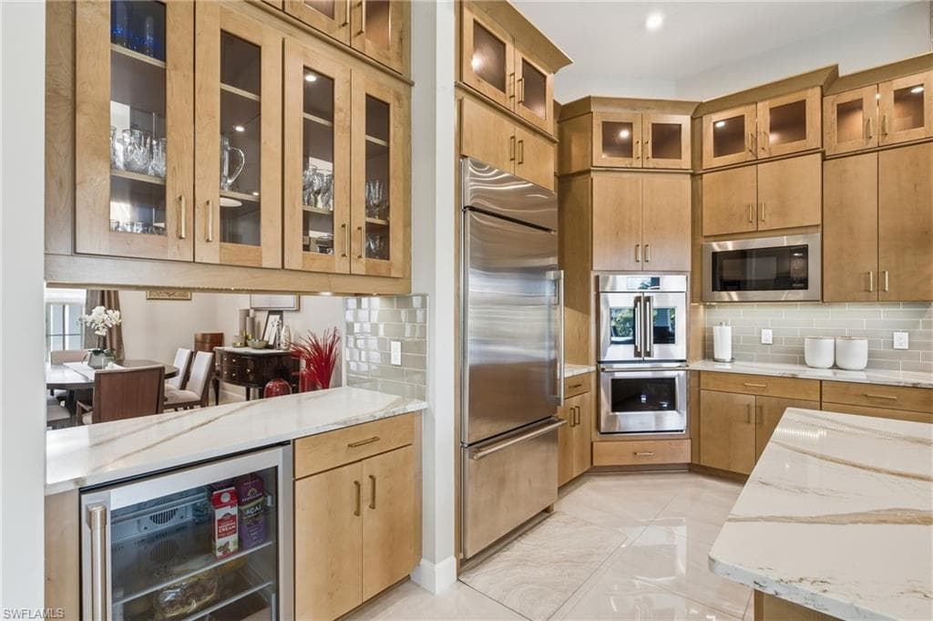 Gourmet kitchen with light wood-finish cabinetry, stainless steel appliances, and polished stone countertops