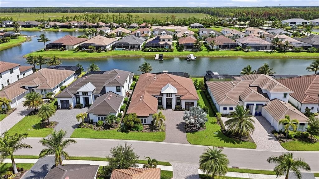 Waterfront property featuring a paver driveway, lush green lawns, mature palm trees, and a private dock