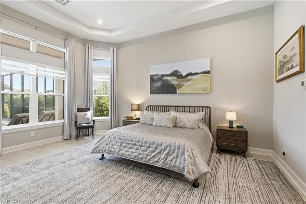 Spacious room featuring tray ceilings, light wood-finish flooring, and expansive windows