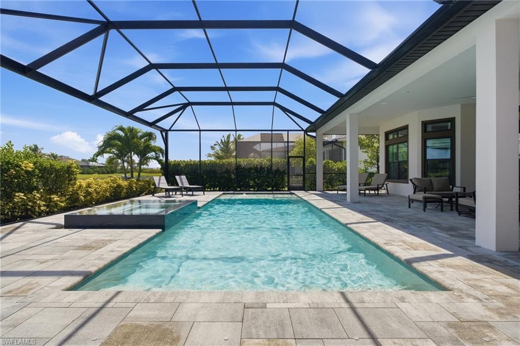 Screened outdoor pool area featuring a rectangular pool, integrated spa, and expansive paver decking