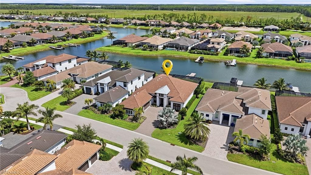 Contemporary single-story residence with a tile roof and light-colored exterior, featuring a paver driveway, mature landscaping, and a private dock on the canal