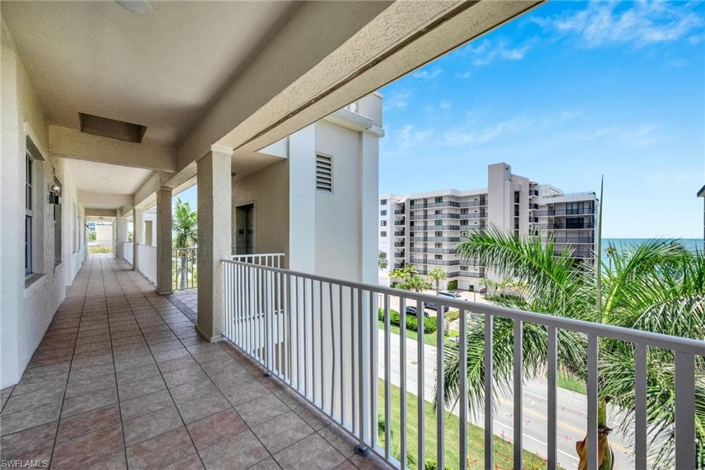 Outdoor walkway featuring tiled flooring and a white railing overlooking a street, palm trees, and the ocean