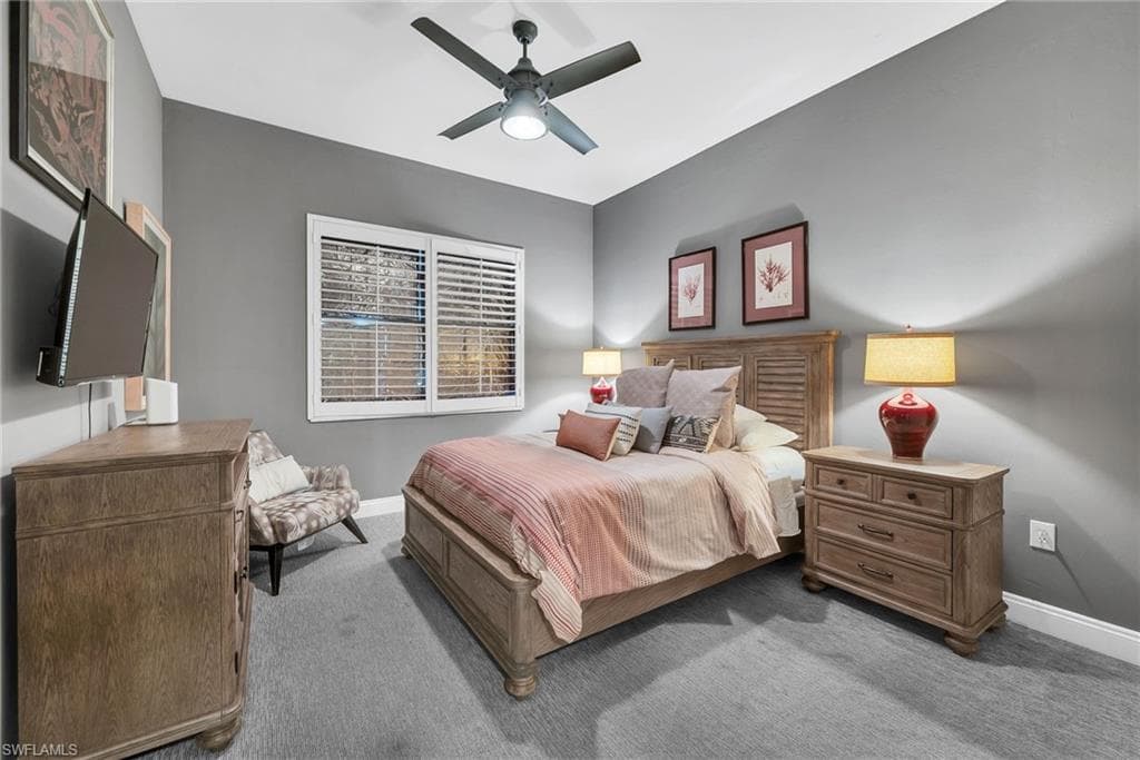 Carpeted bedroom featuring a ceiling fan with integrated lighting, a window with plantation shutters, and a slatted wood-finish headboard