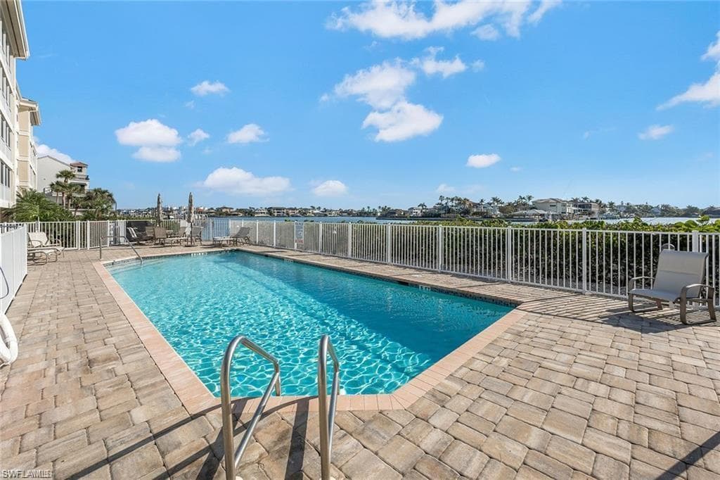 Swimming pool with paver decking, white perimeter fencing, and water frontage