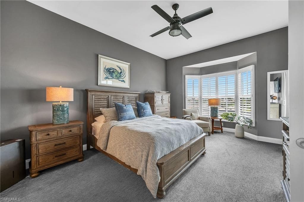 Spacious room featuring a bay window with plantation shutters, ceiling fan, and plush gray carpeting