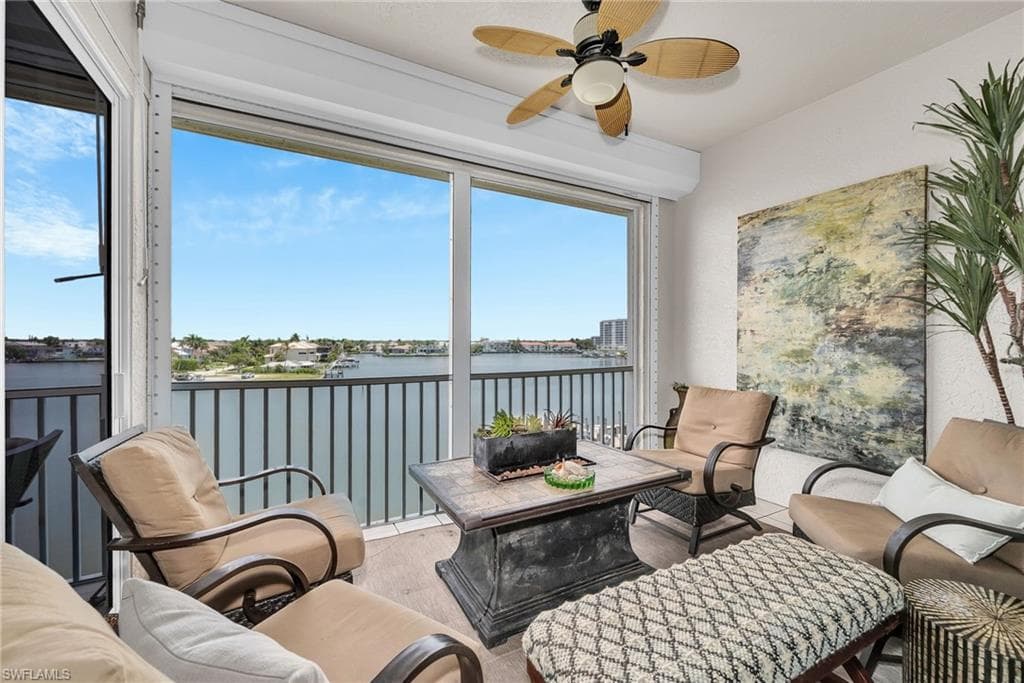 Enclosed balcony featuring expansive water views, sliding glass doors, a ceiling fan, and tile flooring